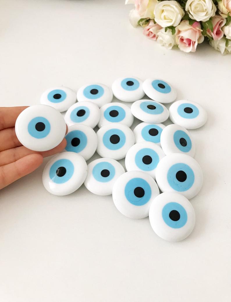 A white handmade evil eye glass bead magnet featuring a traditional Greek design, perfect for home decor and good luck.