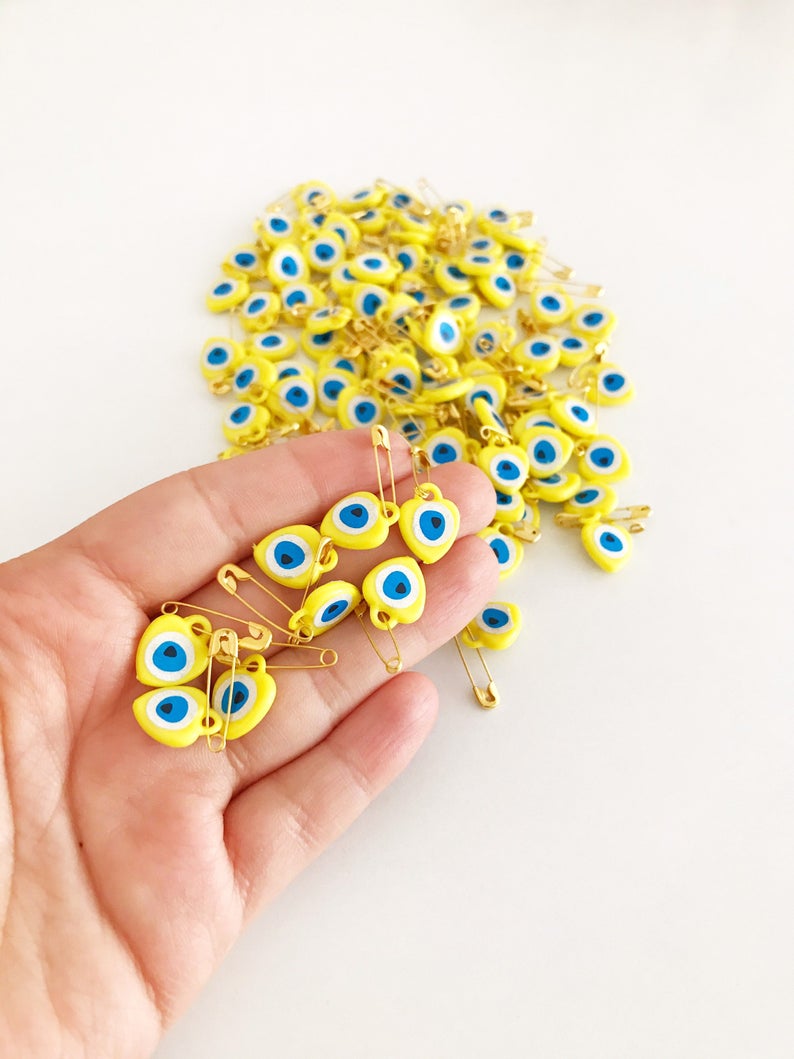 A collection of yellow evil eye beads shaped like hearts, featuring tiny evil eye stickers, displayed on a white background.