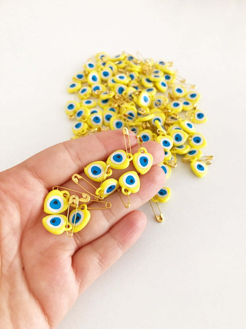 A collection of yellow evil eye beads shaped like hearts, featuring tiny evil eye stickers, displayed on a white background.