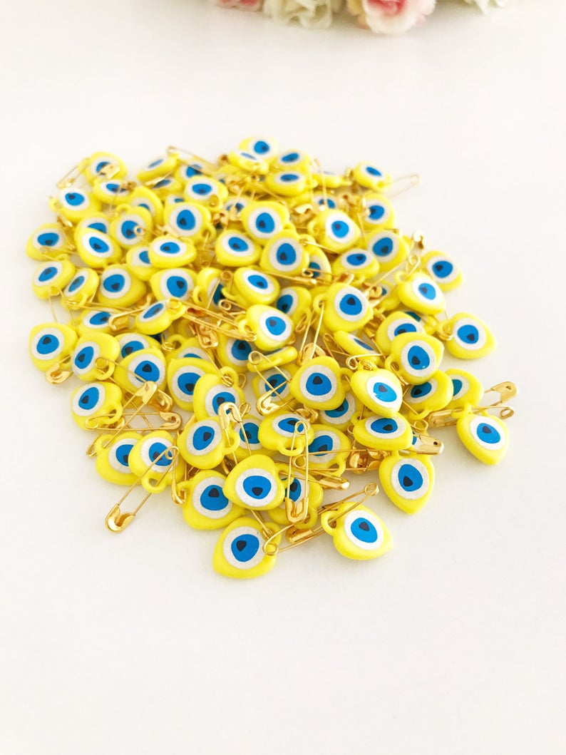 A collection of yellow evil eye beads shaped like hearts, featuring tiny evil eye stickers, displayed on a white background.