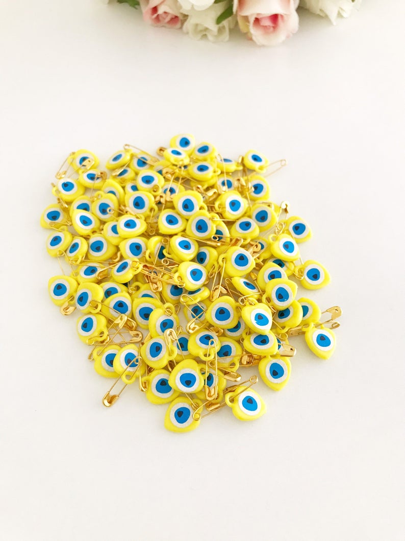 A collection of yellow evil eye beads shaped like hearts, featuring tiny evil eye stickers, displayed on a white background.