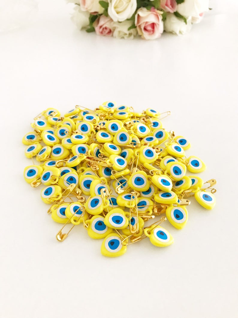 A collection of yellow evil eye beads shaped like hearts, featuring tiny evil eye stickers, displayed on a white background.