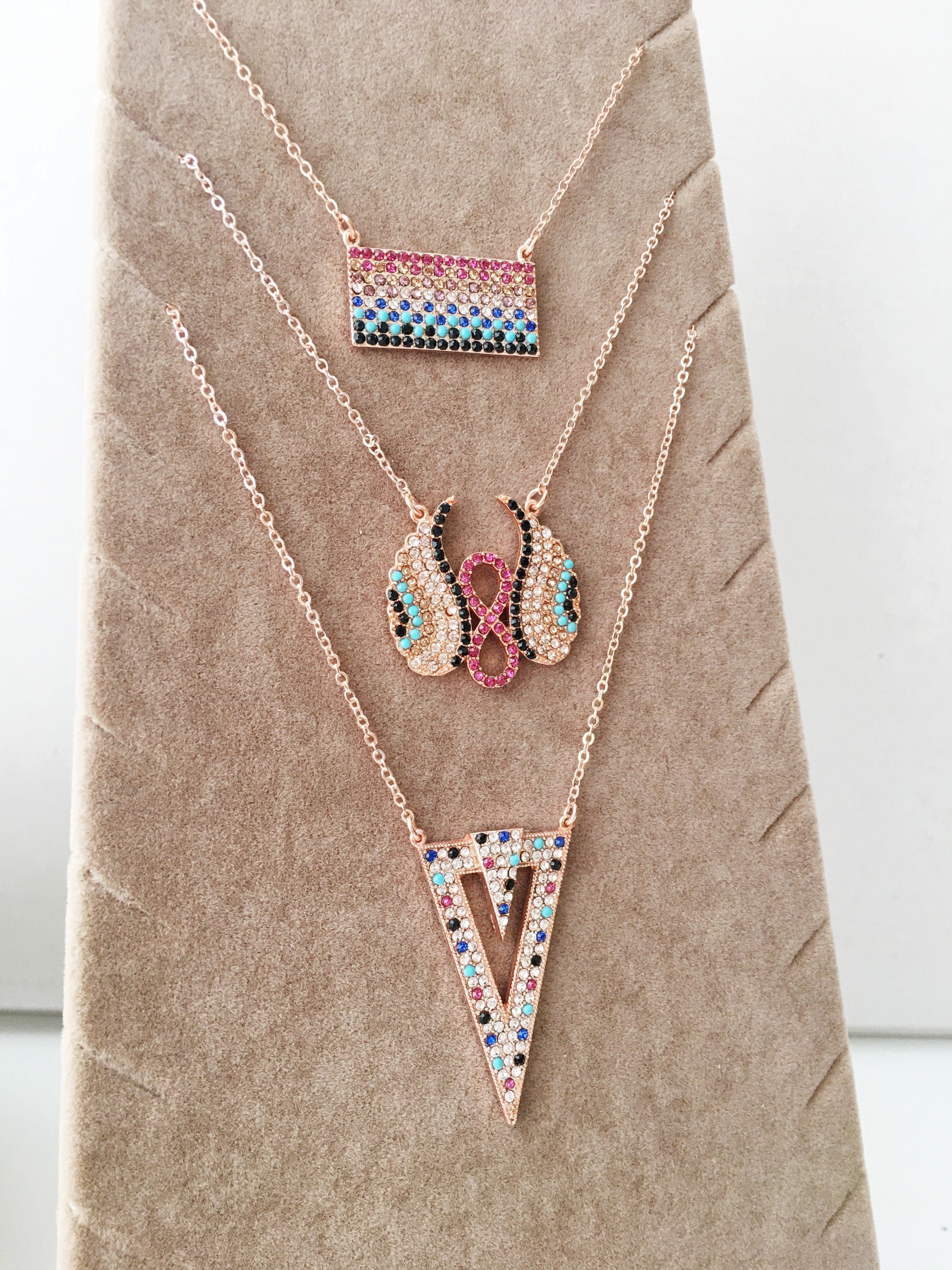 A collection of handmade zirconia necklaces featuring hamsa hand, angel wings, and rectangular designs, crafted in rose gold stainless steel.