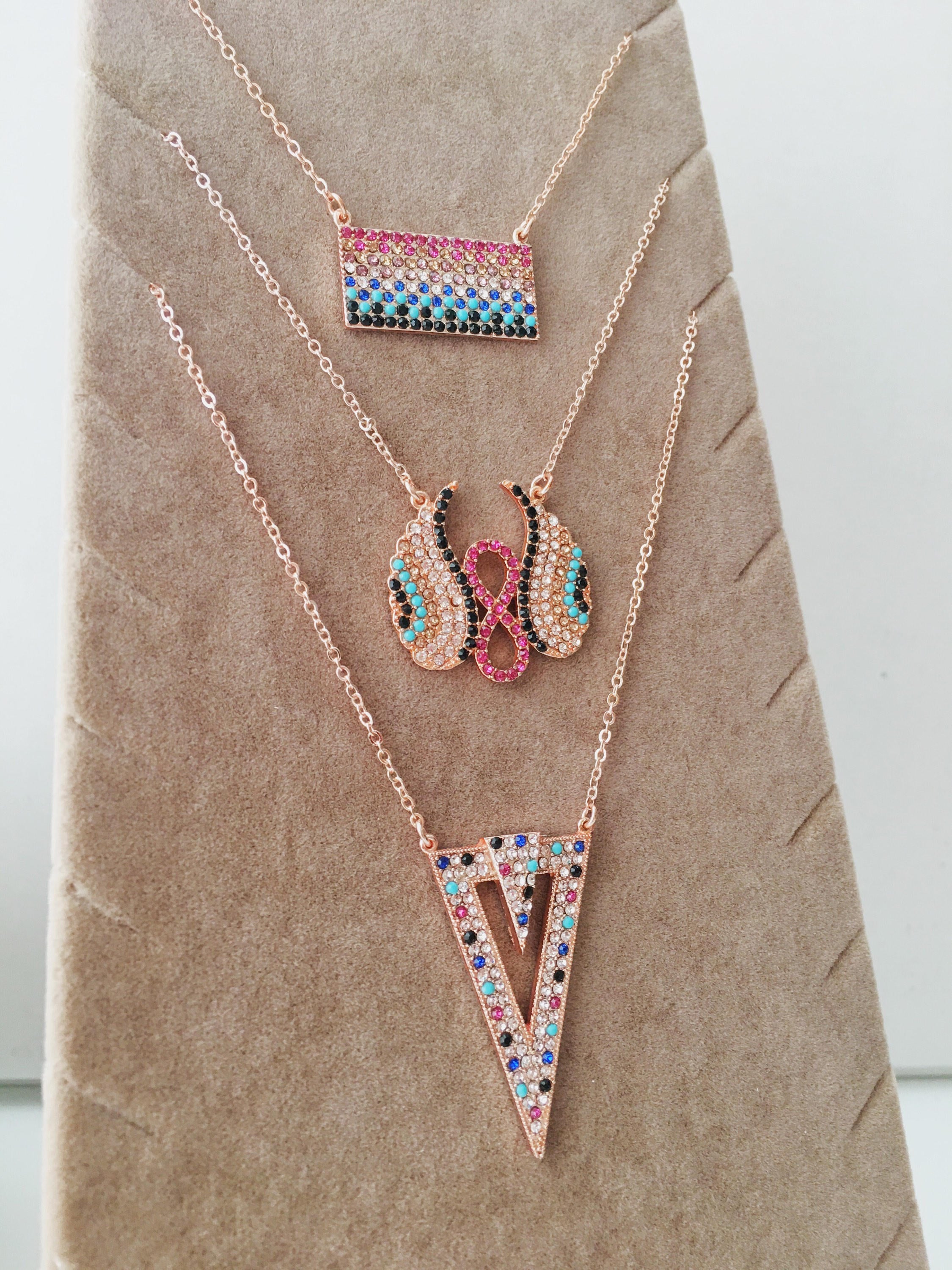 A collection of handmade zirconia necklaces featuring hamsa hand, angel wings, and rectangular designs, crafted in rose gold stainless steel.