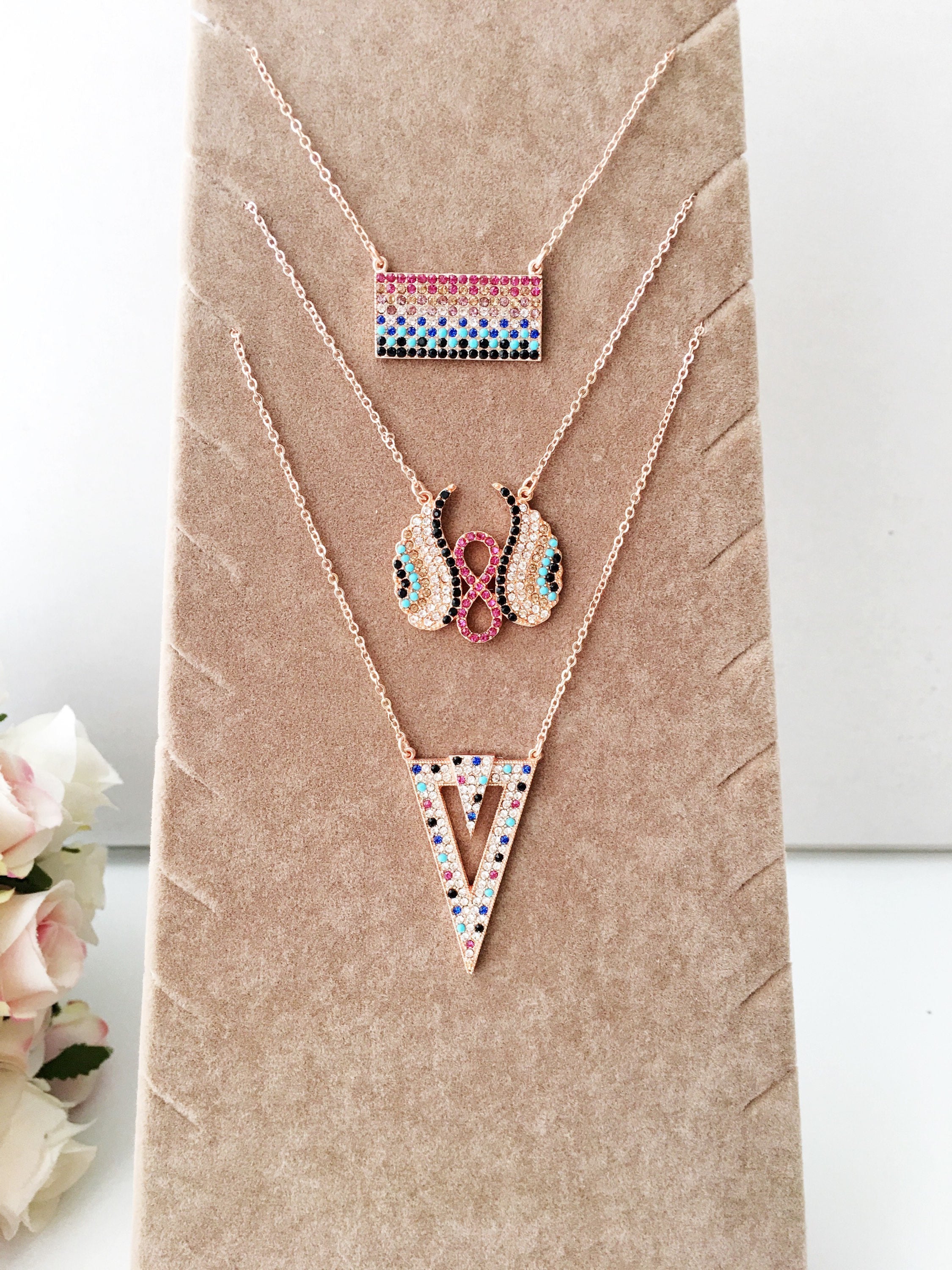 A collection of handmade zirconia necklaces featuring hamsa hand, angel wings, and rectangular designs, crafted in rose gold stainless steel.