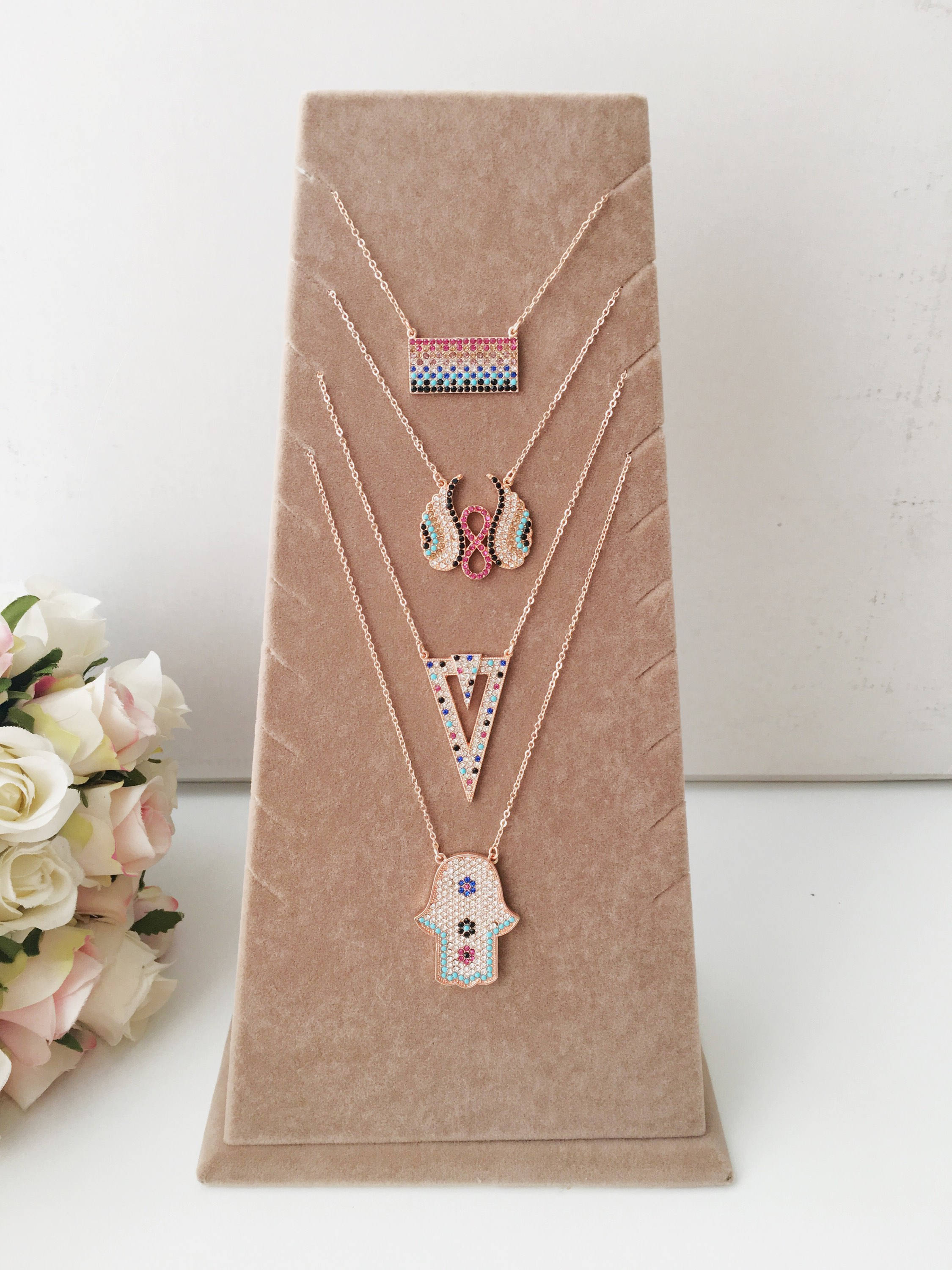 A collection of handmade zirconia necklaces featuring hamsa hand, angel wings, and rectangular designs, crafted in rose gold stainless steel.