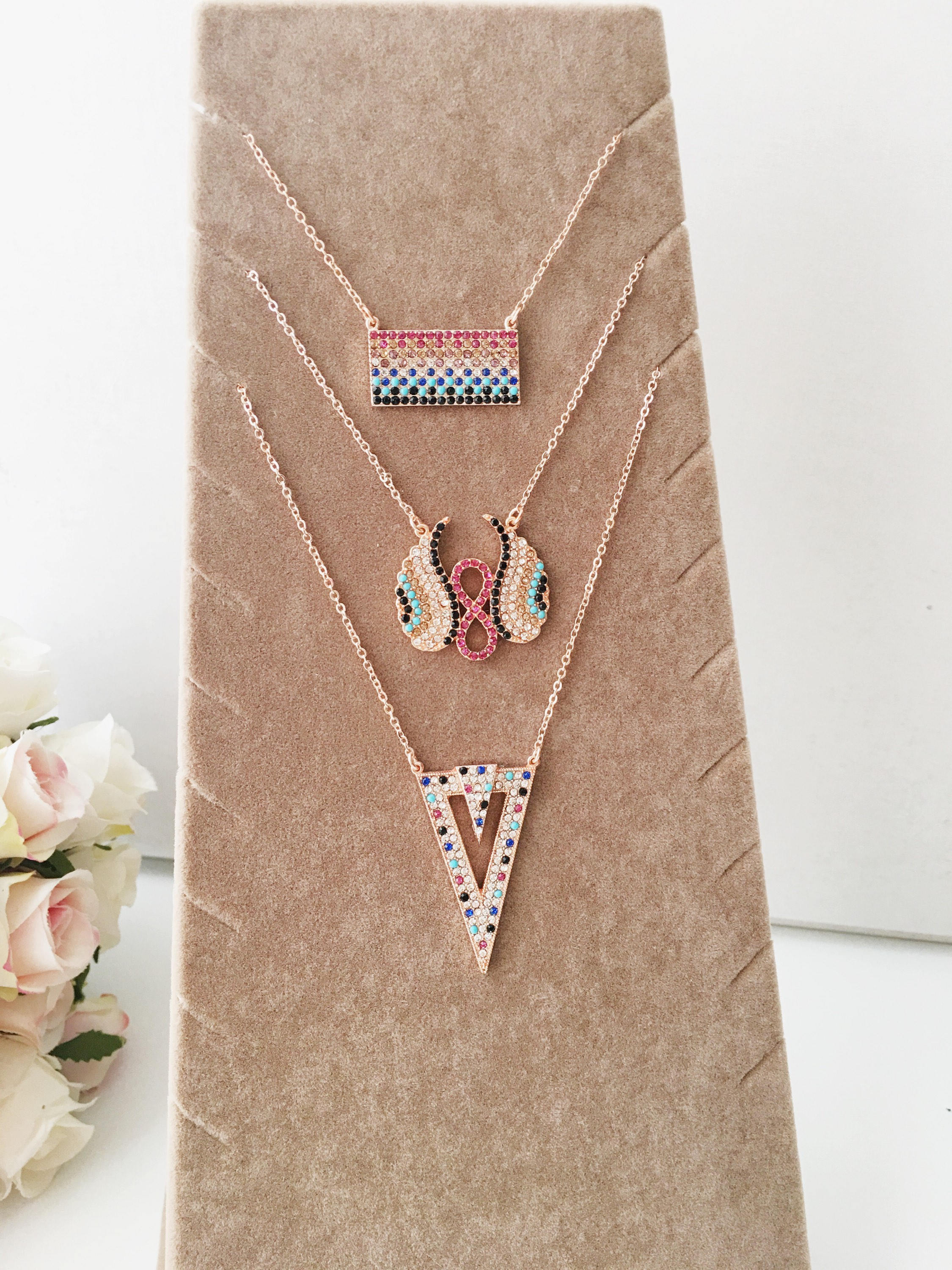 A collection of handmade zirconia necklaces featuring hamsa hand, angel wings, and rectangular designs, crafted in rose gold stainless steel.