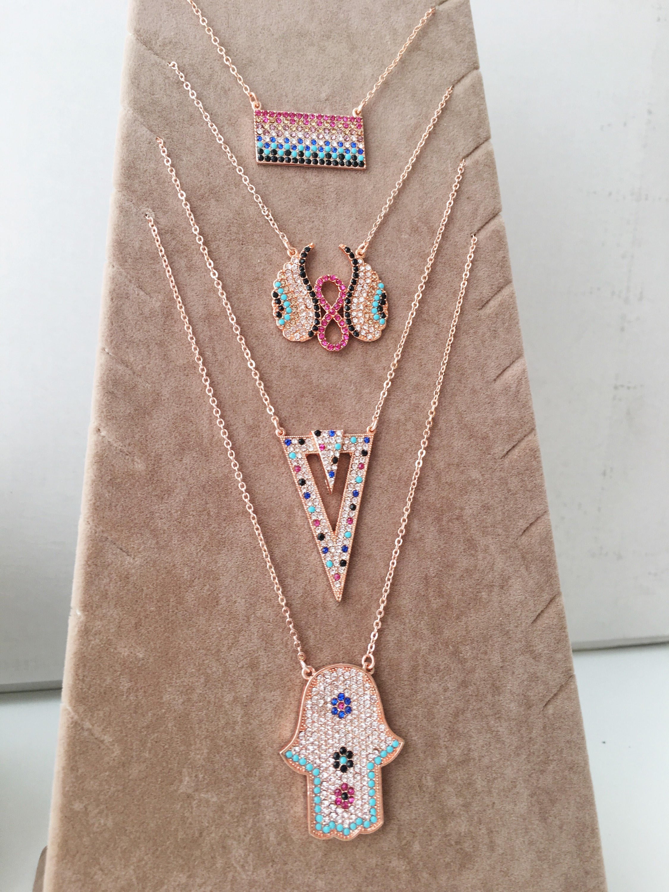 A collection of handmade zirconia necklaces featuring hamsa hand, angel wings, and rectangular designs, crafted in rose gold stainless steel.