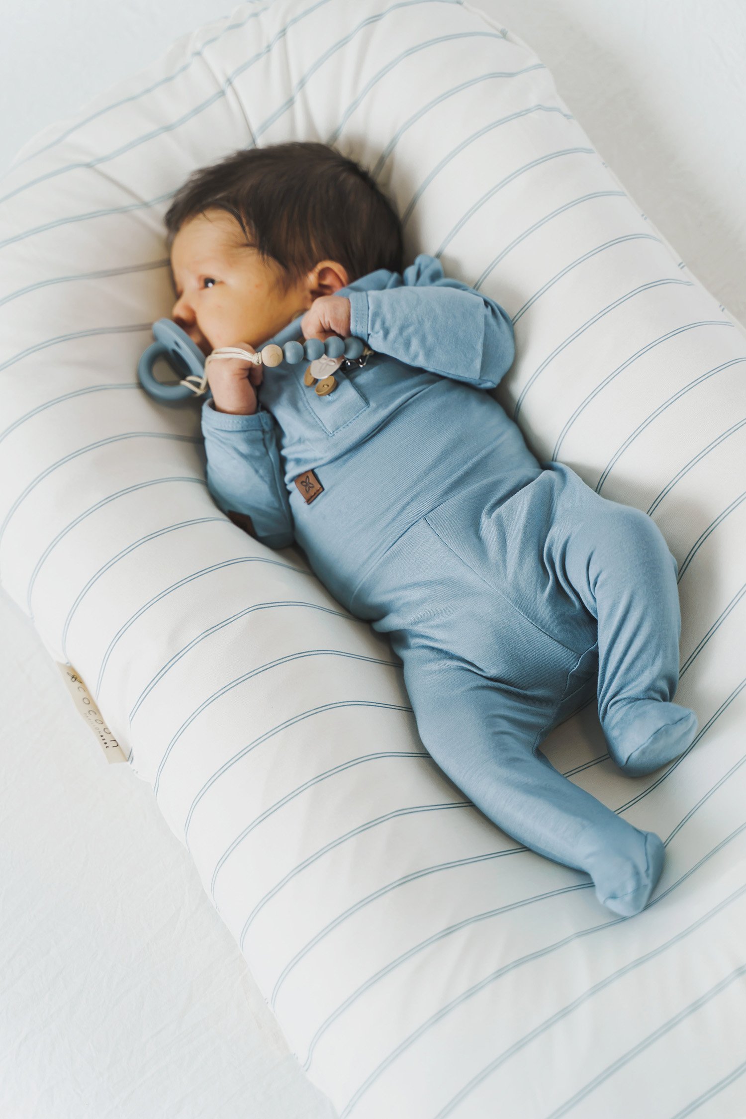 A cozy COCOON & COVER baby lounger in a soft color, featuring a removable liner and a custom-fit traveling case, designed for infants aged 0-36 months.