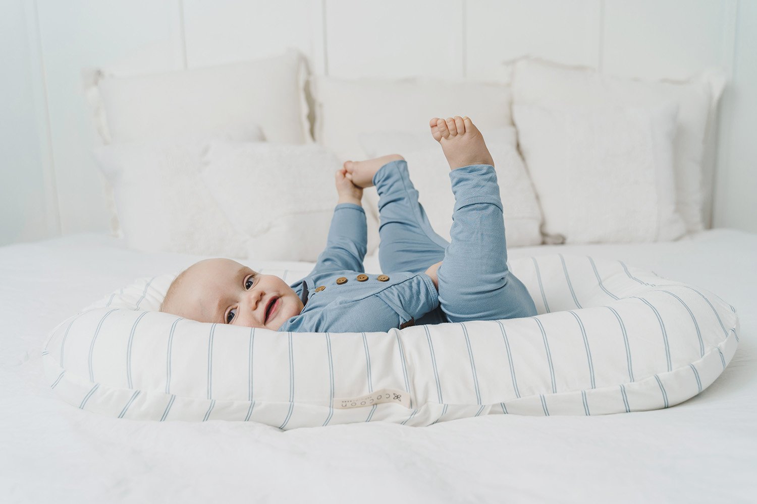 A cozy COCOON & COVER baby lounger in a soft color, featuring a removable liner and a custom-fit traveling case, designed for infants aged 0-36 months.