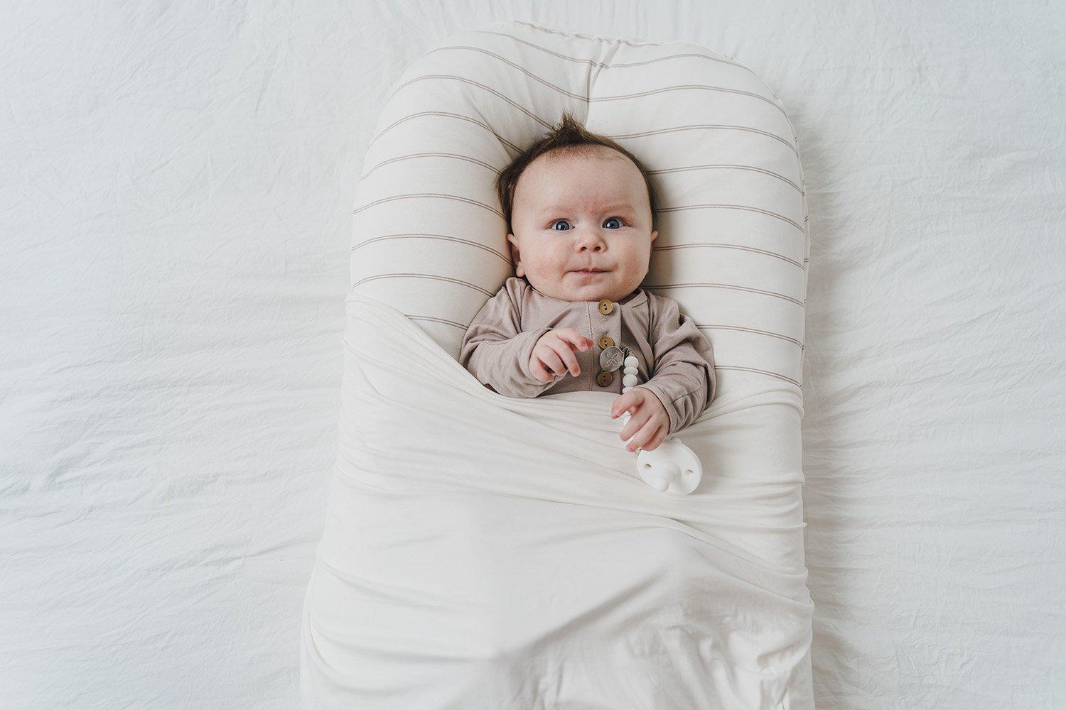 A cozy COCOON & COVER baby lounger in a soft color, featuring a removable liner and a custom-fit traveling case, designed for infants aged 0-36 months.