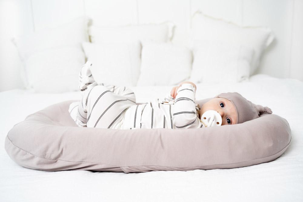 A cozy COCOON & COVER baby lounger in a soft color, featuring a removable liner and a custom-fit traveling case, designed for infants aged 0-36 months.