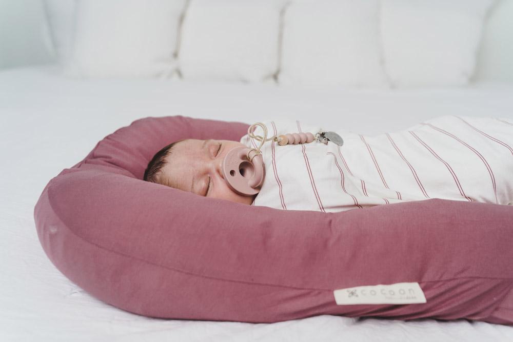 A cozy COCOON & COVER baby lounger in a soft color, featuring a removable liner and a custom-fit traveling case, designed for infants aged 0-36 months.