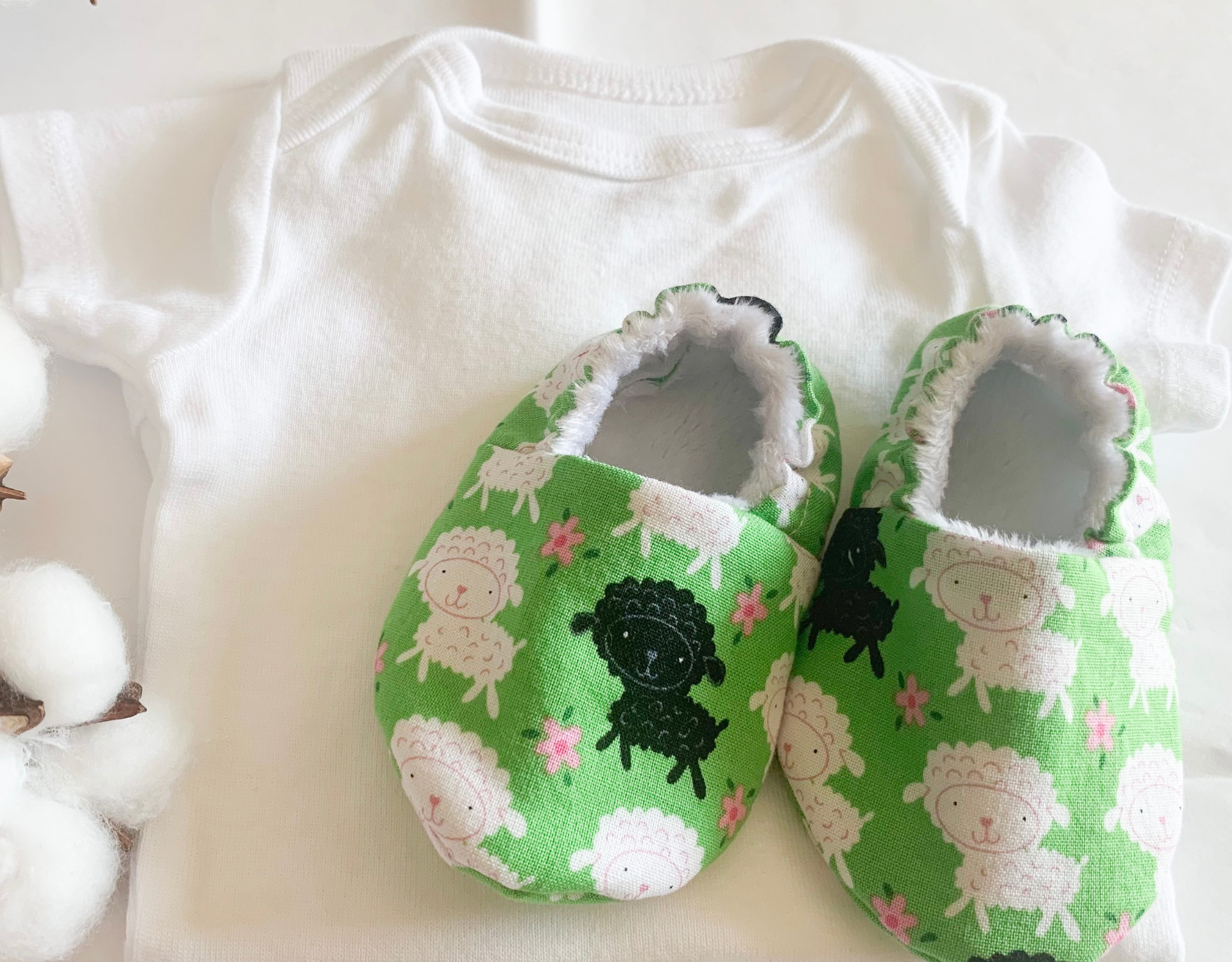 Lamb Elastic Baby Shoe featuring black and white lambs on a green background with soft minky fleece lining.