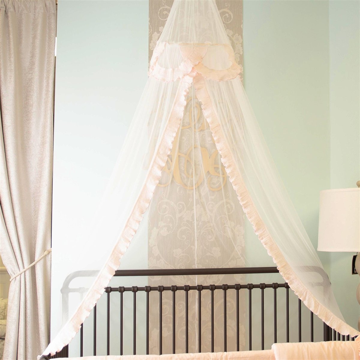 A beautiful blush pink lace tulle canopy draped over a crib, creating a dreamy nursery atmosphere.