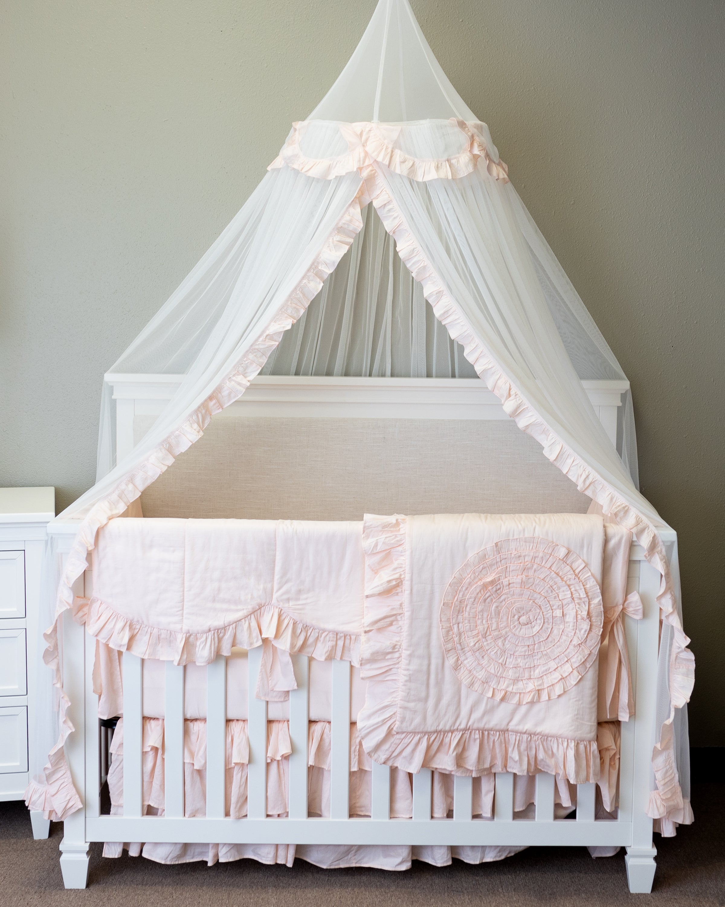 A beautiful blush pink lace tulle canopy draped over a crib, creating a dreamy nursery atmosphere.