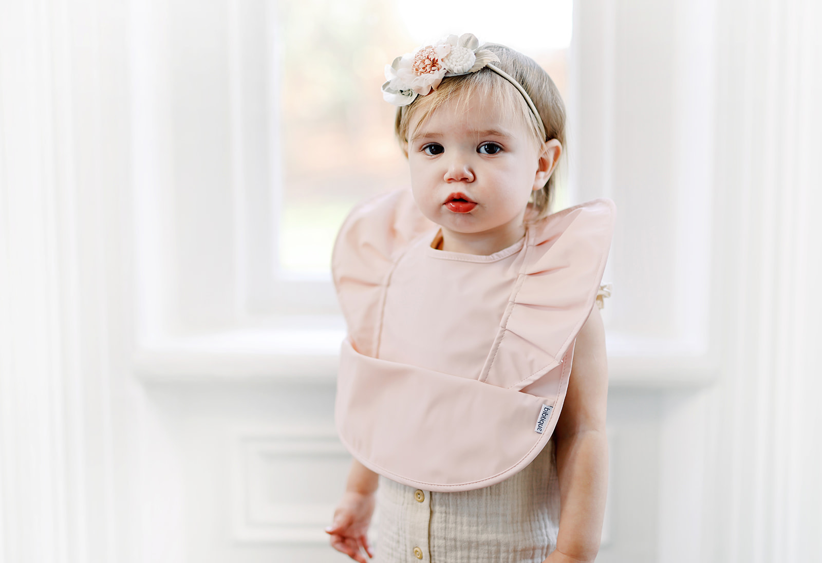 Peach Blush Ruffle Angel Bib showcasing its elegant design and practical features, perfect for baby mealtime.