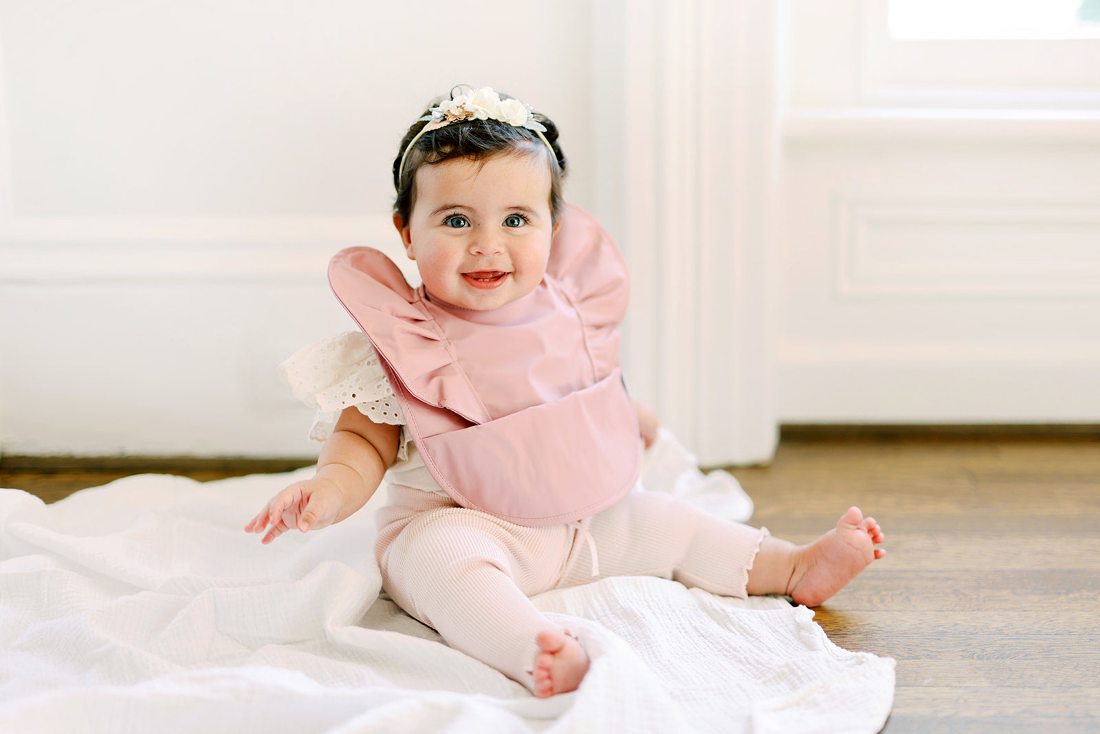 Peony Ruffle Angel Bib featuring a beautiful floral design, soft material, and a built-in pocket for spills.