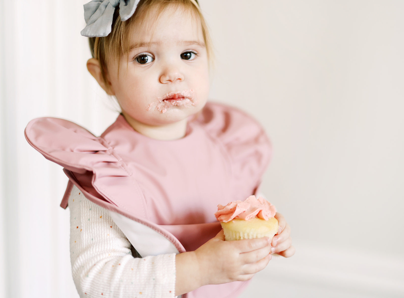 Peony Ruffle Angel Bib featuring a beautiful floral design, soft material, and a built-in pocket for spills.