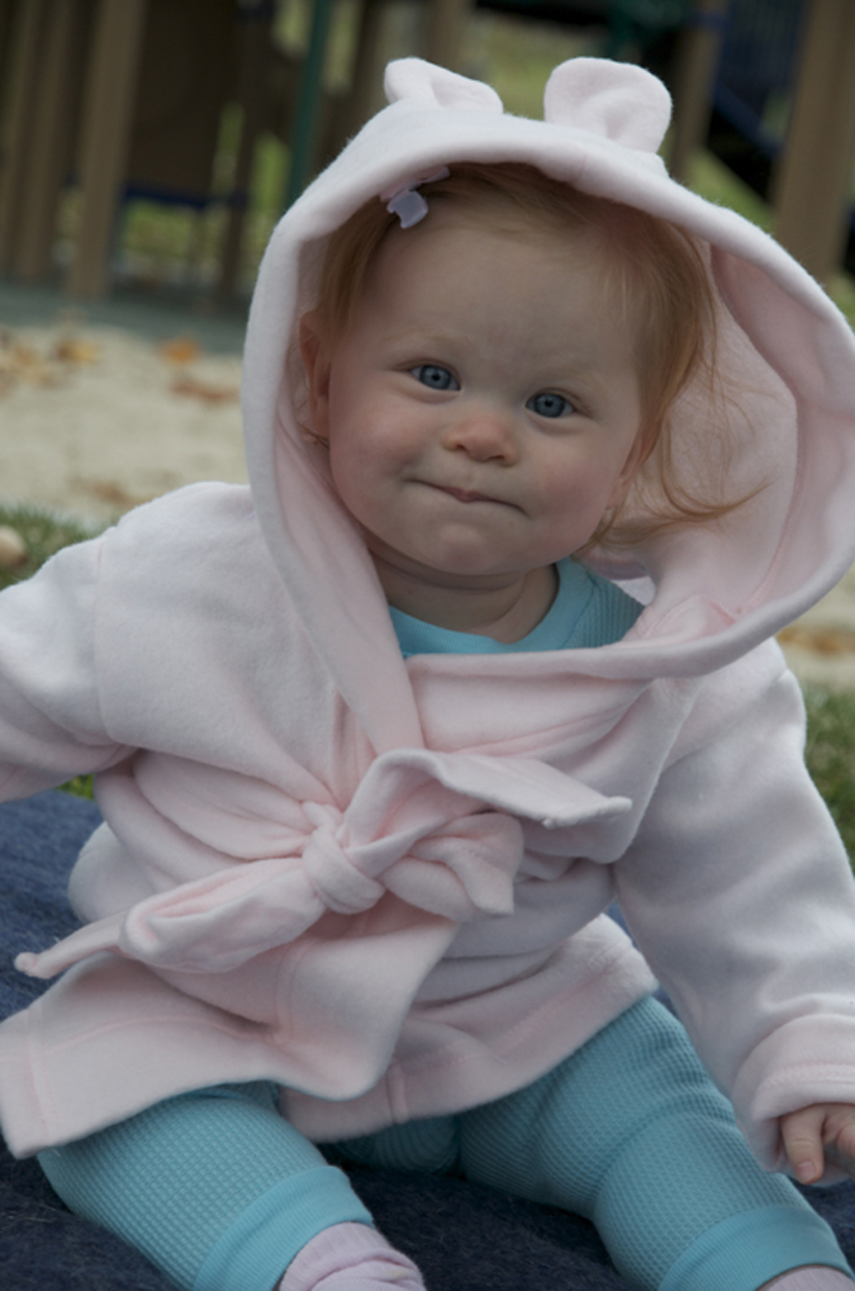 A pink fleece robe with a hoodie featuring cute rabbit ears, designed for newborns, showcasing its soft texture and playful design.