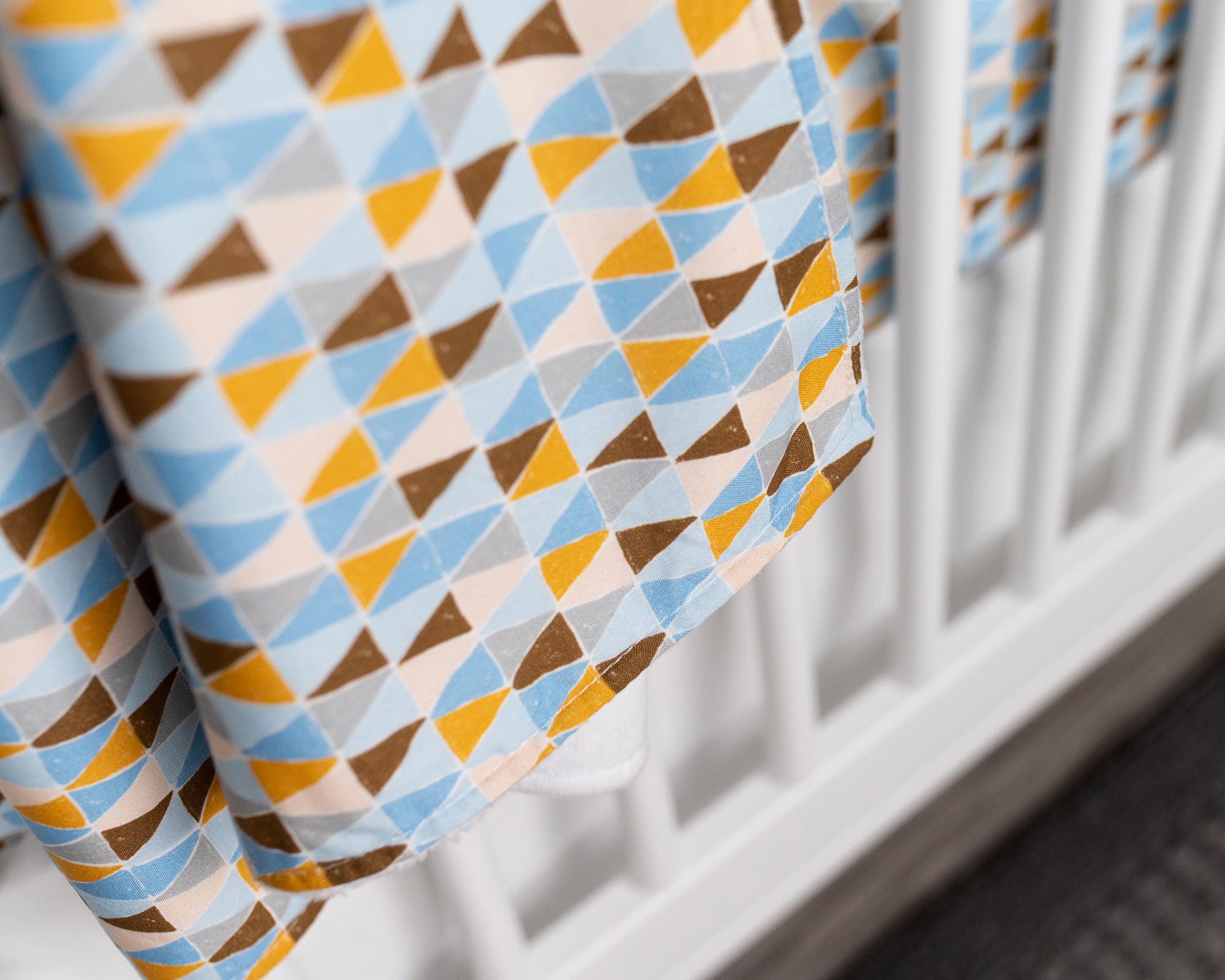 Blue Banners Marching Classic Crib Bedding Set featuring vibrant triangles in blue, brown, gray, and mustard colors, made from premium cotton.