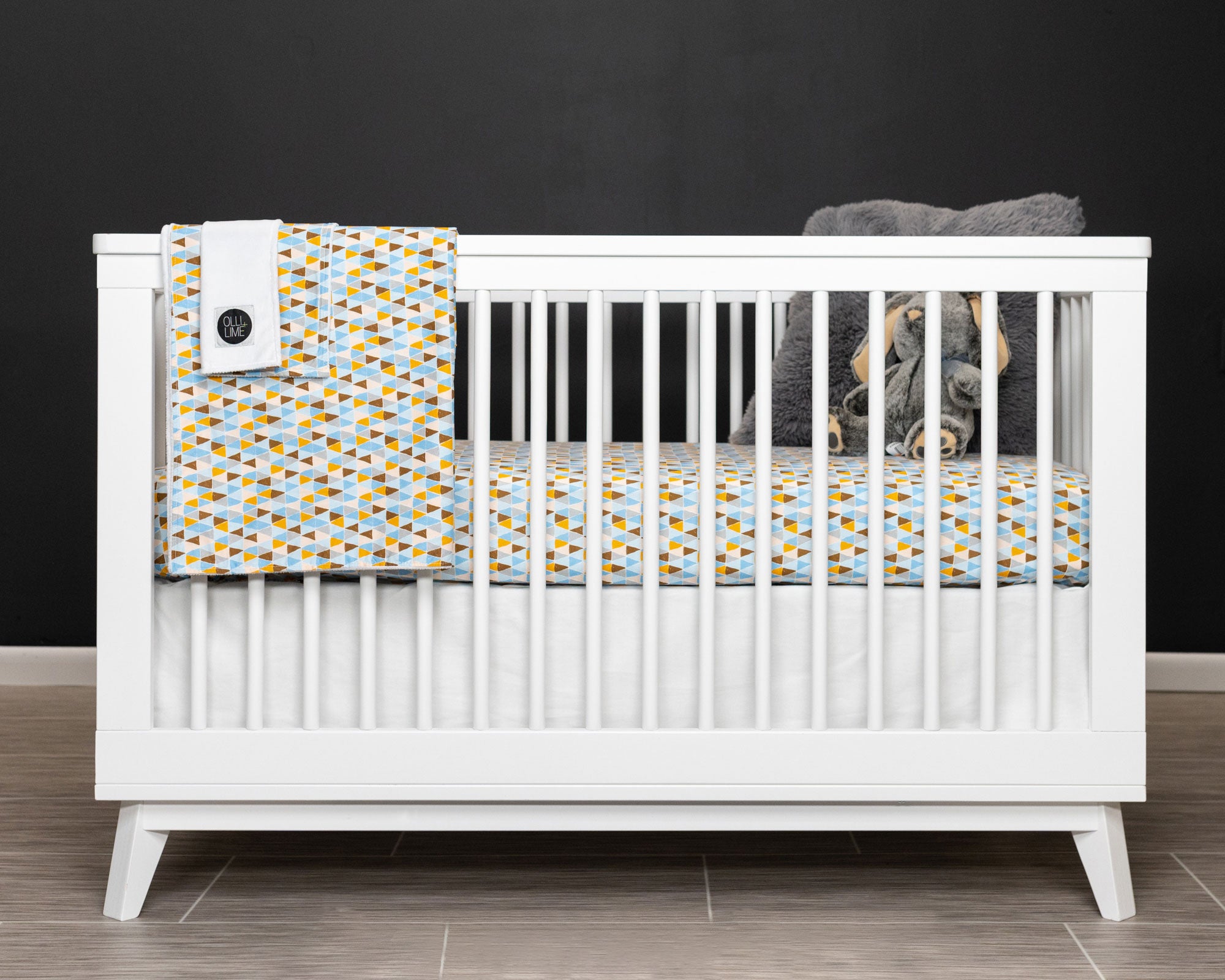 Blue Banners Marching Deluxe Crib Bedding Set featuring blue, brown, gray, and mustard triangles with a white crib skirt and baby blankets.