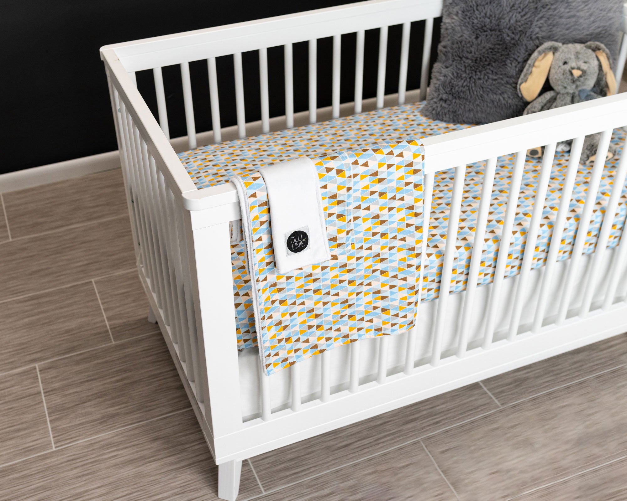 Blue Banners Marching Deluxe Crib Bedding Set featuring blue, brown, gray, and mustard triangles with a white crib skirt and baby blankets.