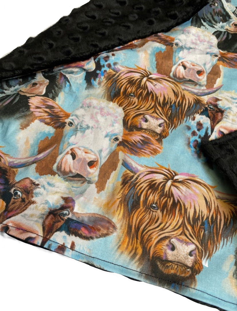 Highland cow lovey blanket featuring a mix of shaggy cows on a light blue background with a soft black bubble minky backing, perfect for babies.