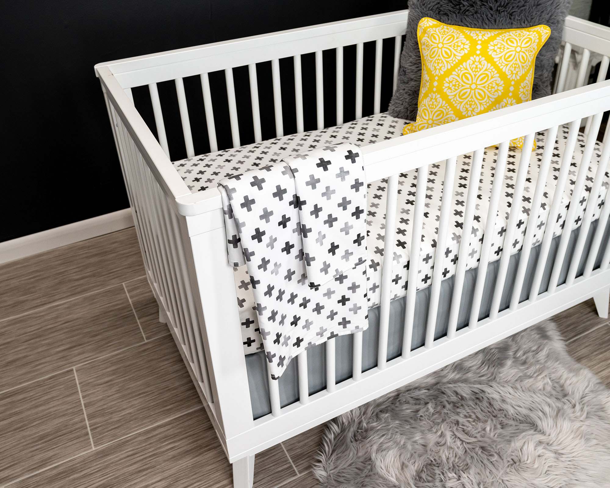 Hugo's Hazy Cross Deluxe Crib Bedding Set featuring gray Swiss cross pattern on white background, includes crib skirt, fitted sheet, baby blanket, and lovey.