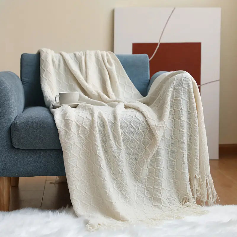 A beautifully knitted beige decorative blanket with geometric patterns and rolled fringed edges, showcasing its luxurious texture and craftsmanship.