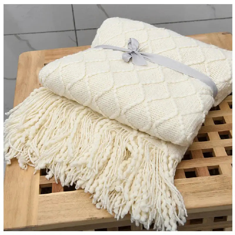 A beautifully knitted beige decorative blanket with geometric patterns and rolled fringed edges, showcasing its luxurious texture and craftsmanship.