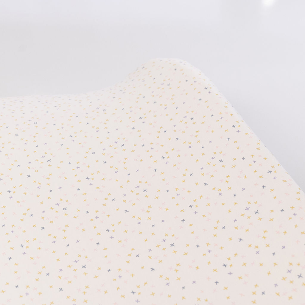 Olli+Lime Little Tiny Hugs Changing Pad Cover featuring delicate X's in blue, green, and pink on an ivory background, perfect for a nursery.