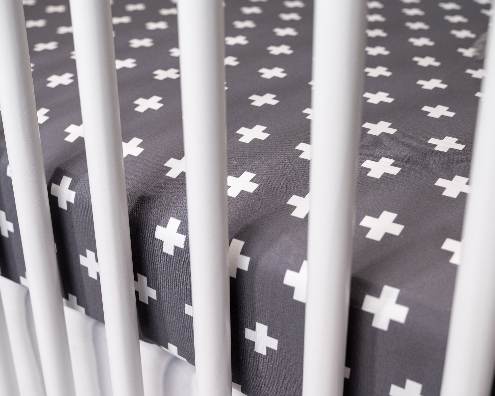 Nils Fitted Crib Sheet featuring a stylish white Swiss cross pattern on dark gray fabric, designed for modern nurseries.