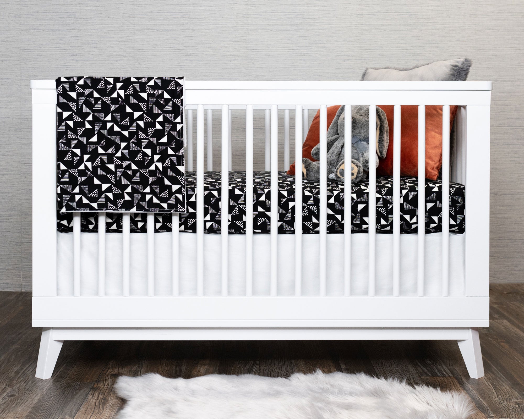 Pinwheels Crib Bedding Set featuring modern triangle patterns in gray and white on a black background, including a crib skirt, fitted sheet, and baby blanket.