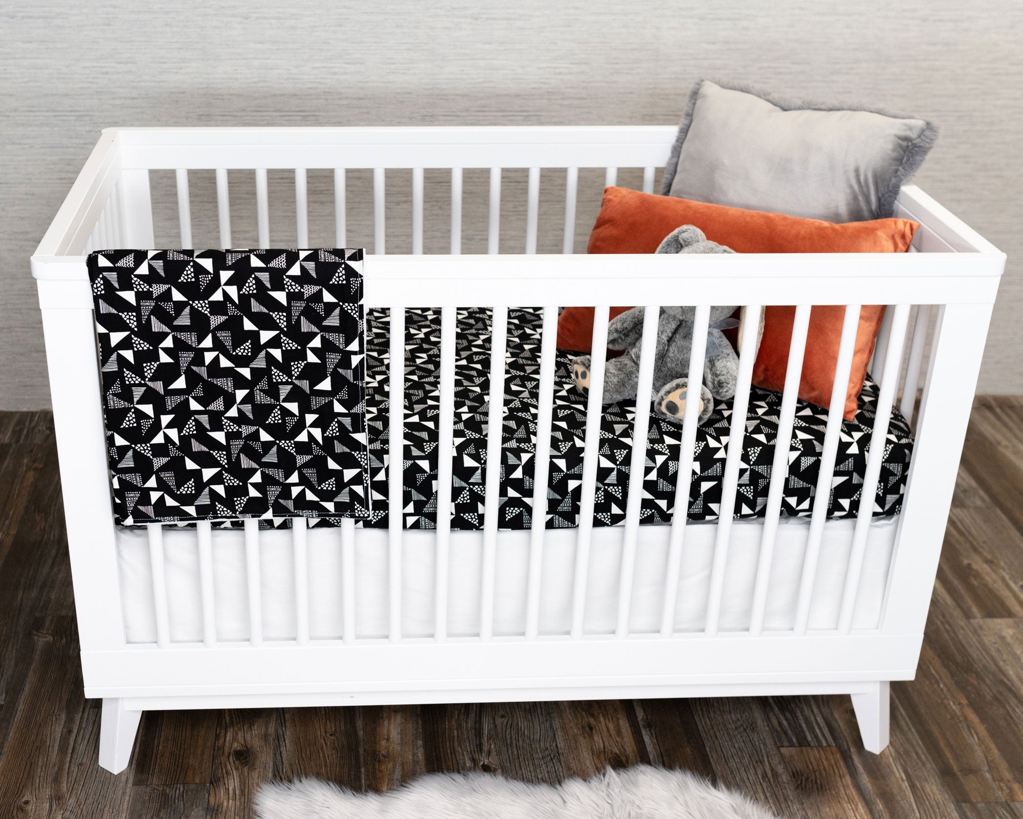 Pinwheels Crib Bedding Set featuring modern triangle patterns in gray and white on a black background, including a crib skirt, fitted sheet, and baby blanket.