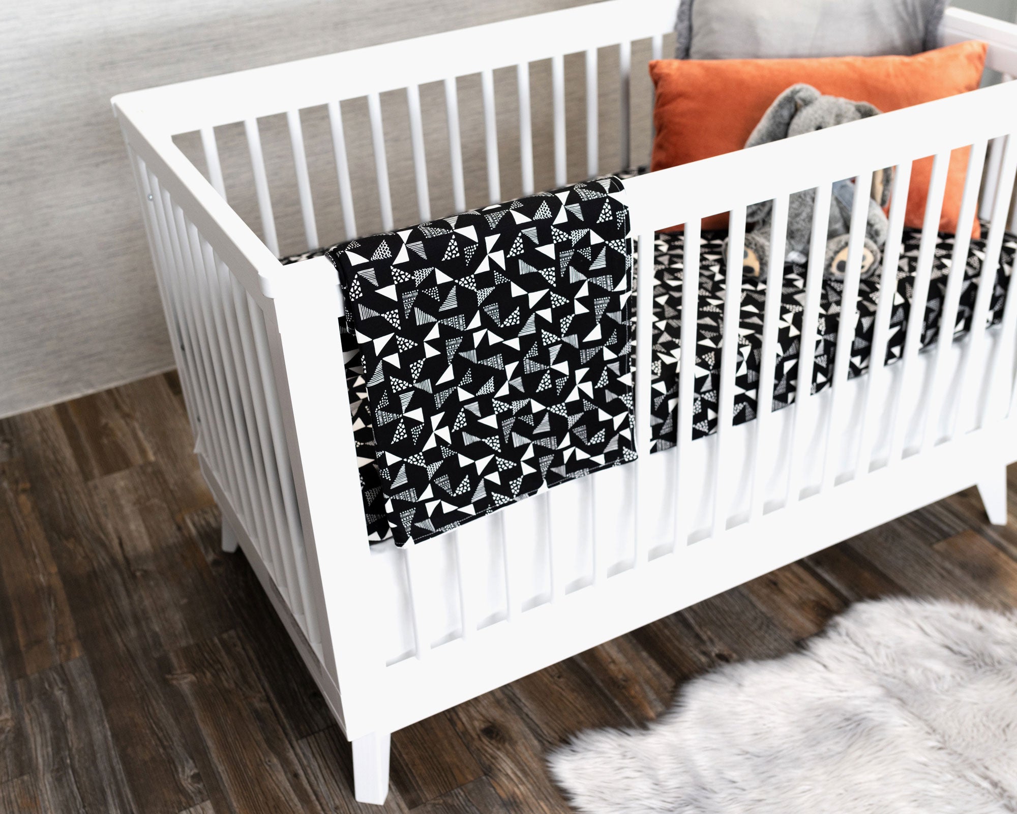 Pinwheels Crib Bedding Set featuring modern triangle patterns in gray and white on a black background, including a crib skirt, fitted sheet, and baby blanket.