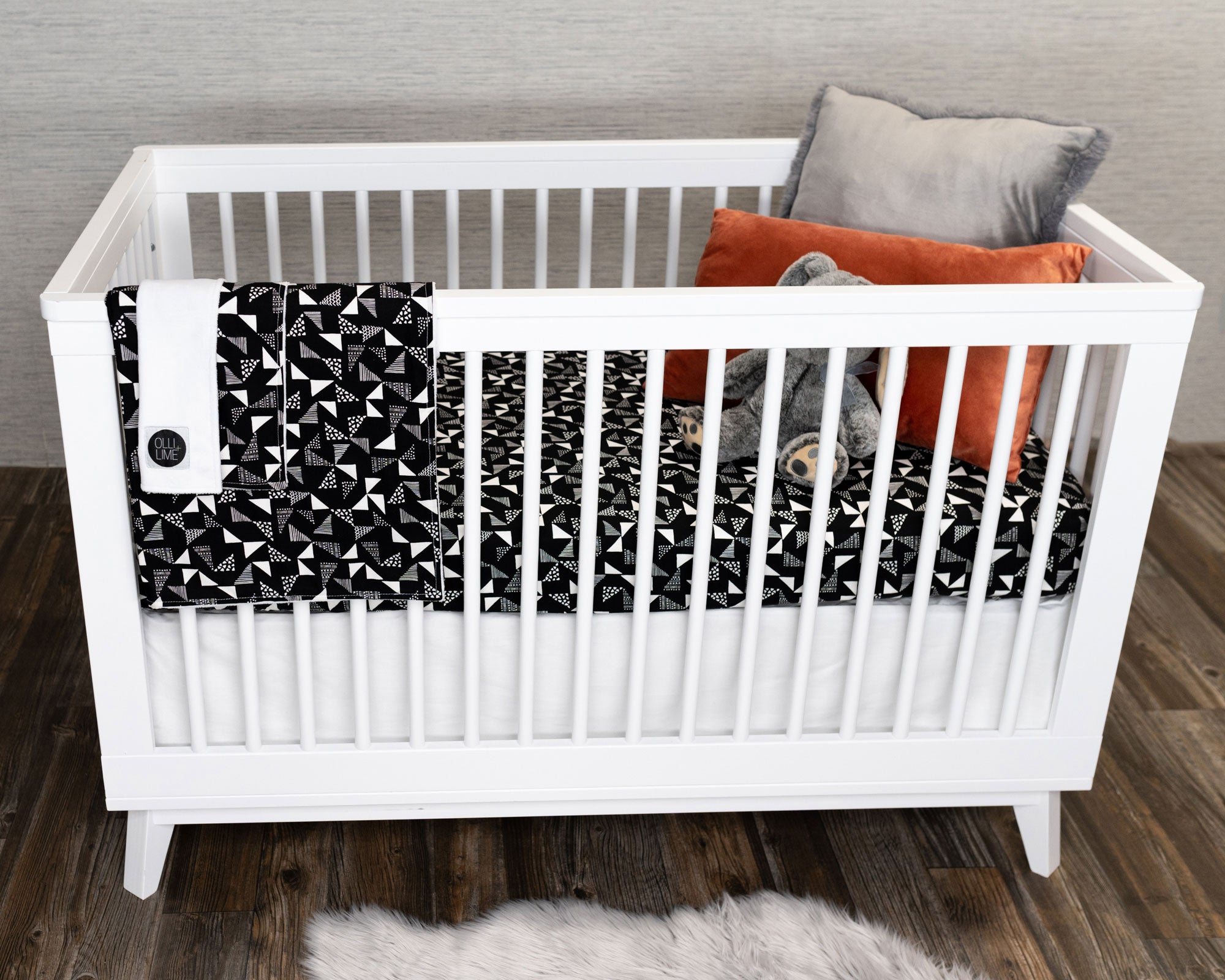 Pinwheels Deluxe Crib Bedding Set featuring gray and white triangles on a black backdrop, including crib skirt, fitted sheet, baby blanket, and lovey.