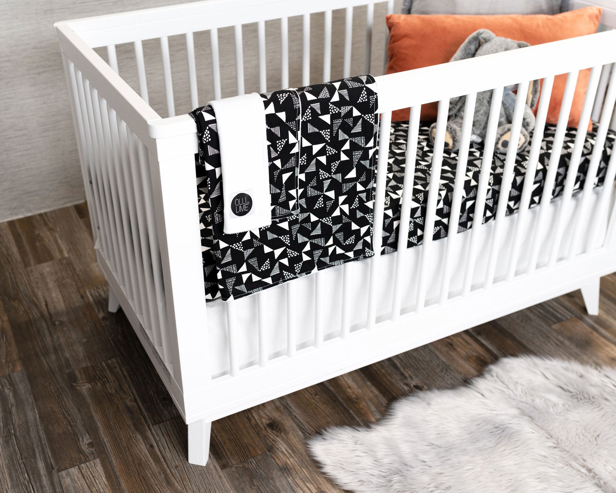 Pinwheels Deluxe Crib Bedding Set featuring gray and white triangles on a black backdrop, including crib skirt, fitted sheet, baby blanket, and lovey.