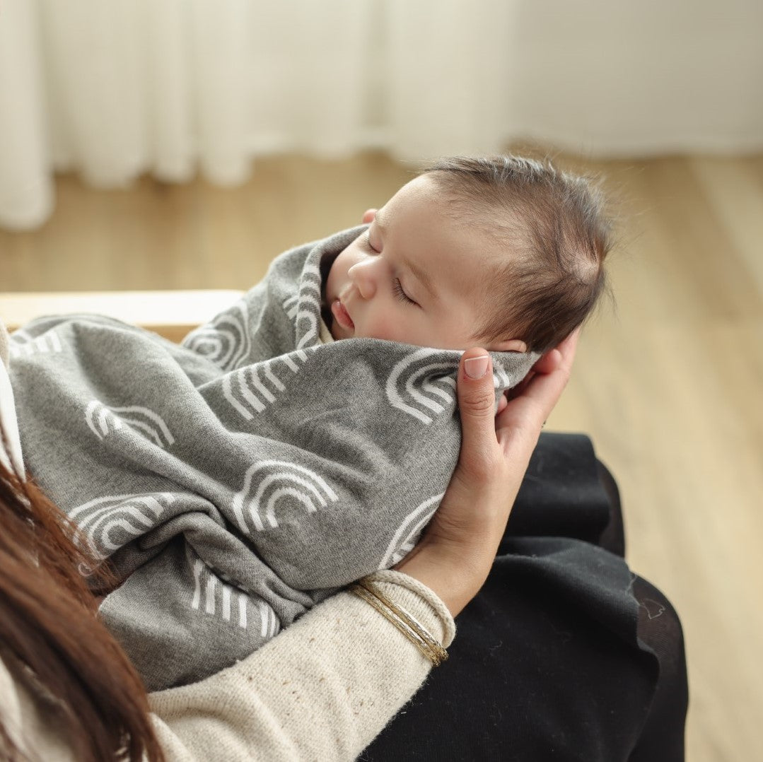 A colorful rainbow knit swaddle blanket made of soft cotton, perfect for wrapping newborns and toddlers, featuring a gentle and breathable design.