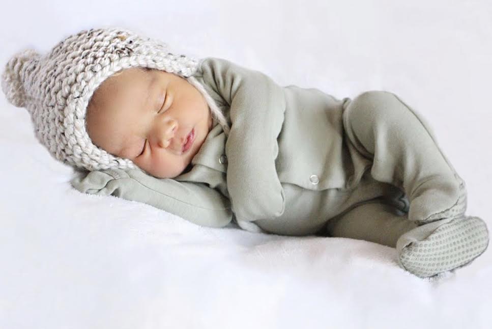 A cozy oatmeal temperance bonnet with a pom detail, showcasing its handmade knit design and stretchy fit.