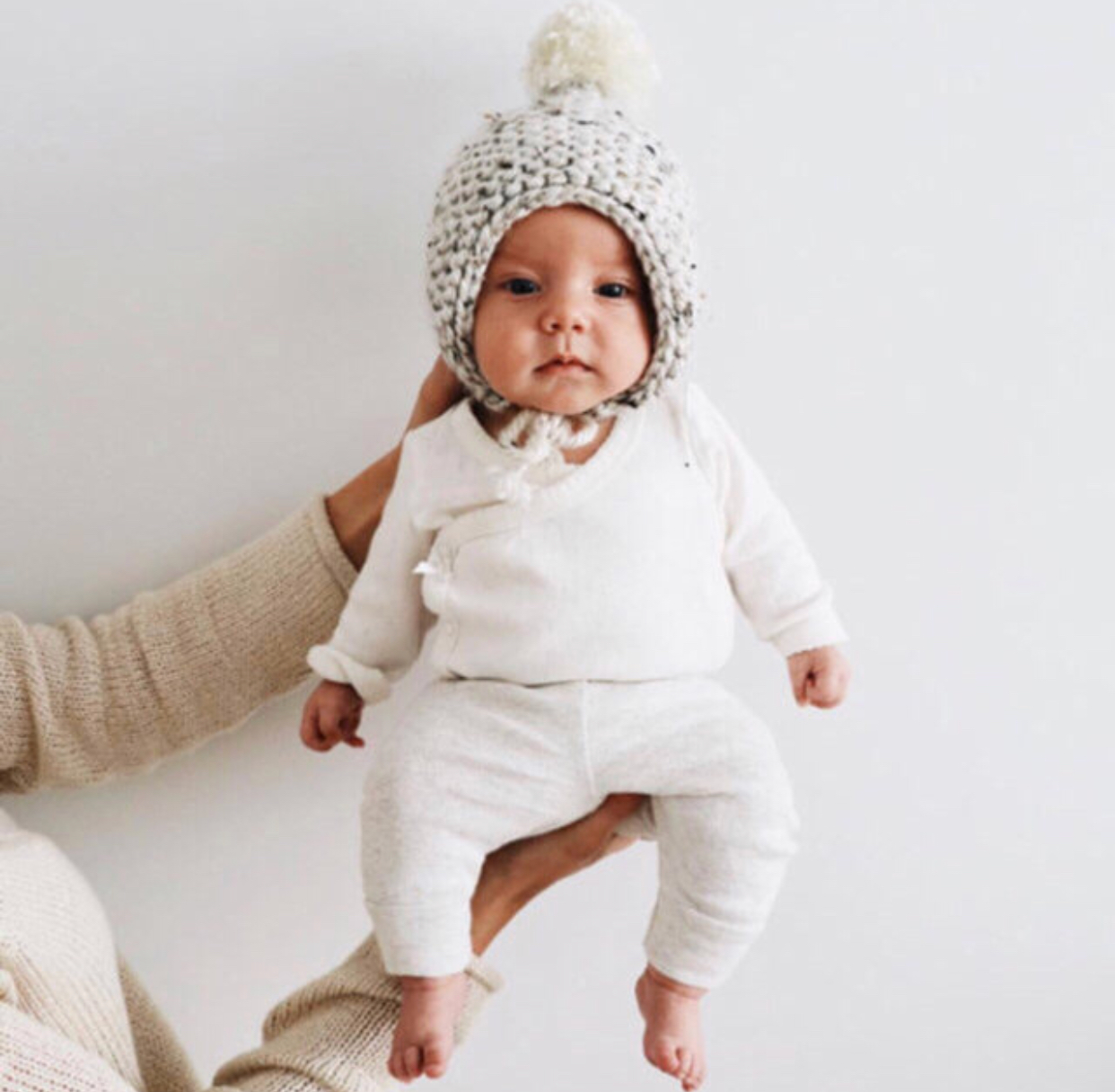 A cozy oatmeal temperance bonnet with a pom detail, showcasing its handmade knit design and stretchy fit.