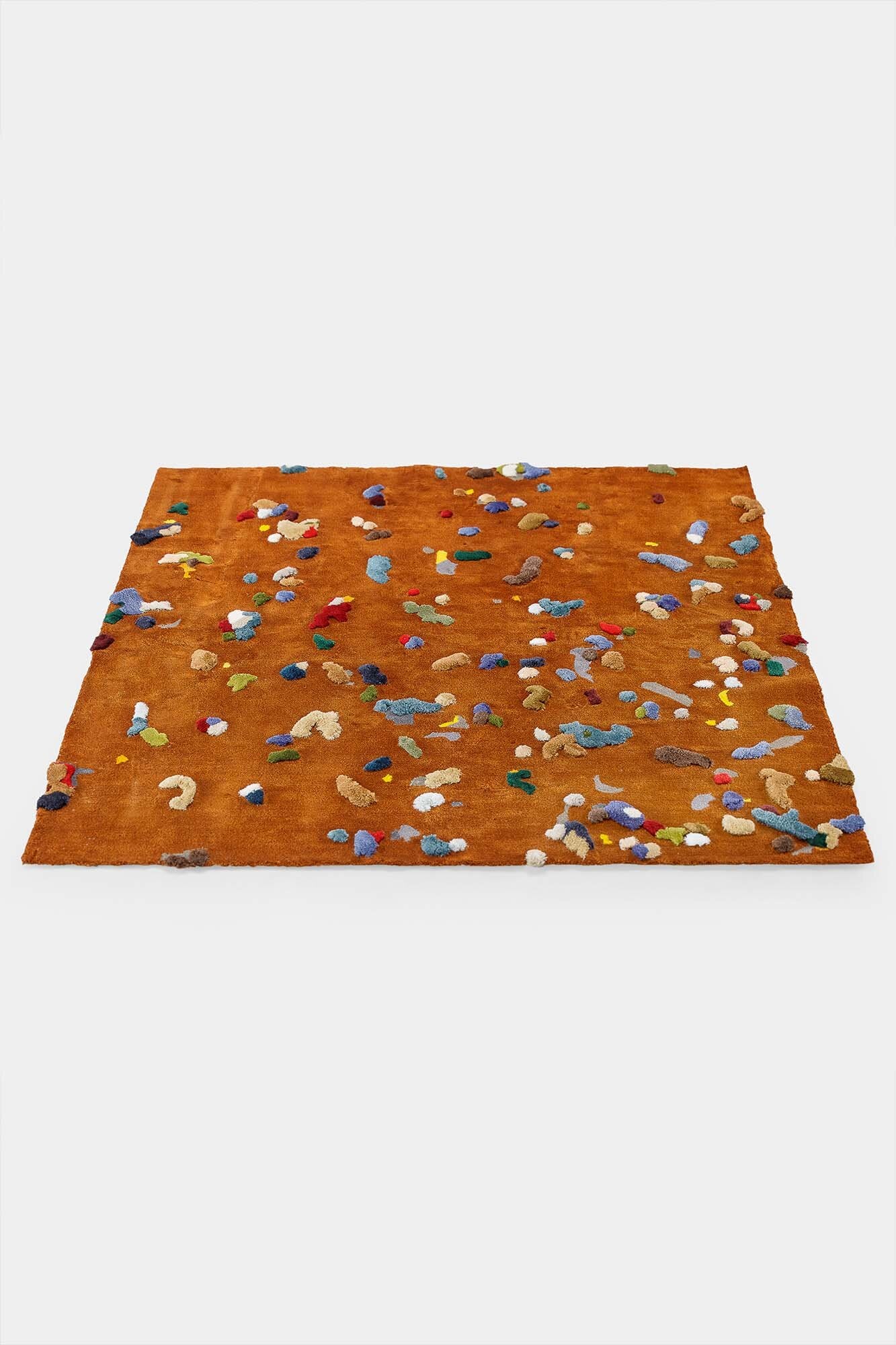 A vibrant Chaos Rug designed by Audronė Drungilaitė, showcasing unique colors and patterns made from leftover yarn, available in dark blue and caramel brown.