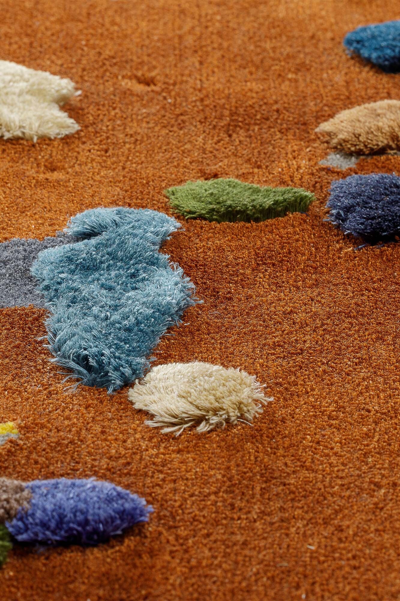 A vibrant Chaos Rug designed by Audronė Drungilaitė, showcasing unique colors and patterns made from leftover yarn, available in dark blue and caramel brown.