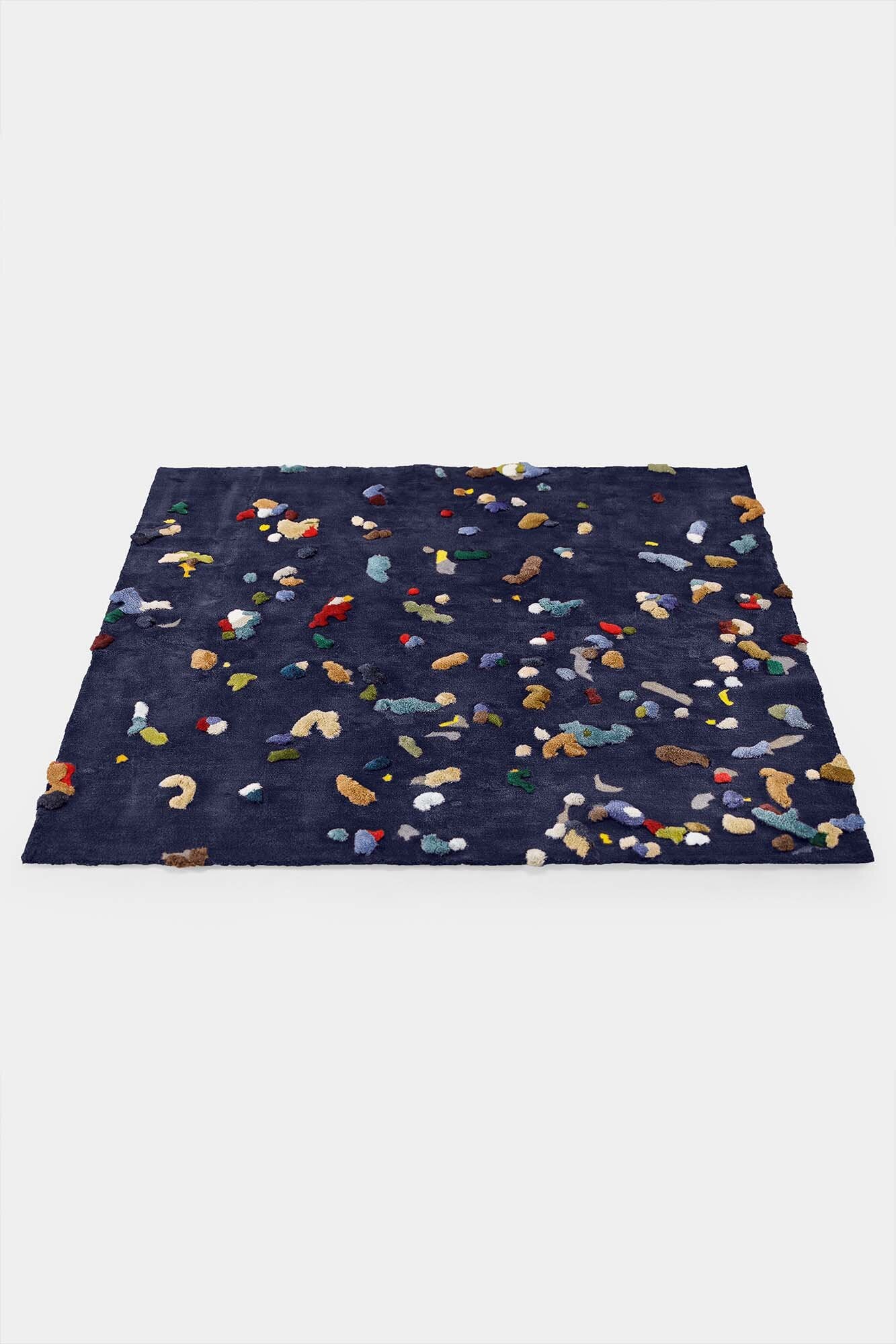 A vibrant Chaos Rug designed by Audronė Drungilaitė, showcasing unique colors and patterns made from leftover yarn, available in dark blue and caramel brown.