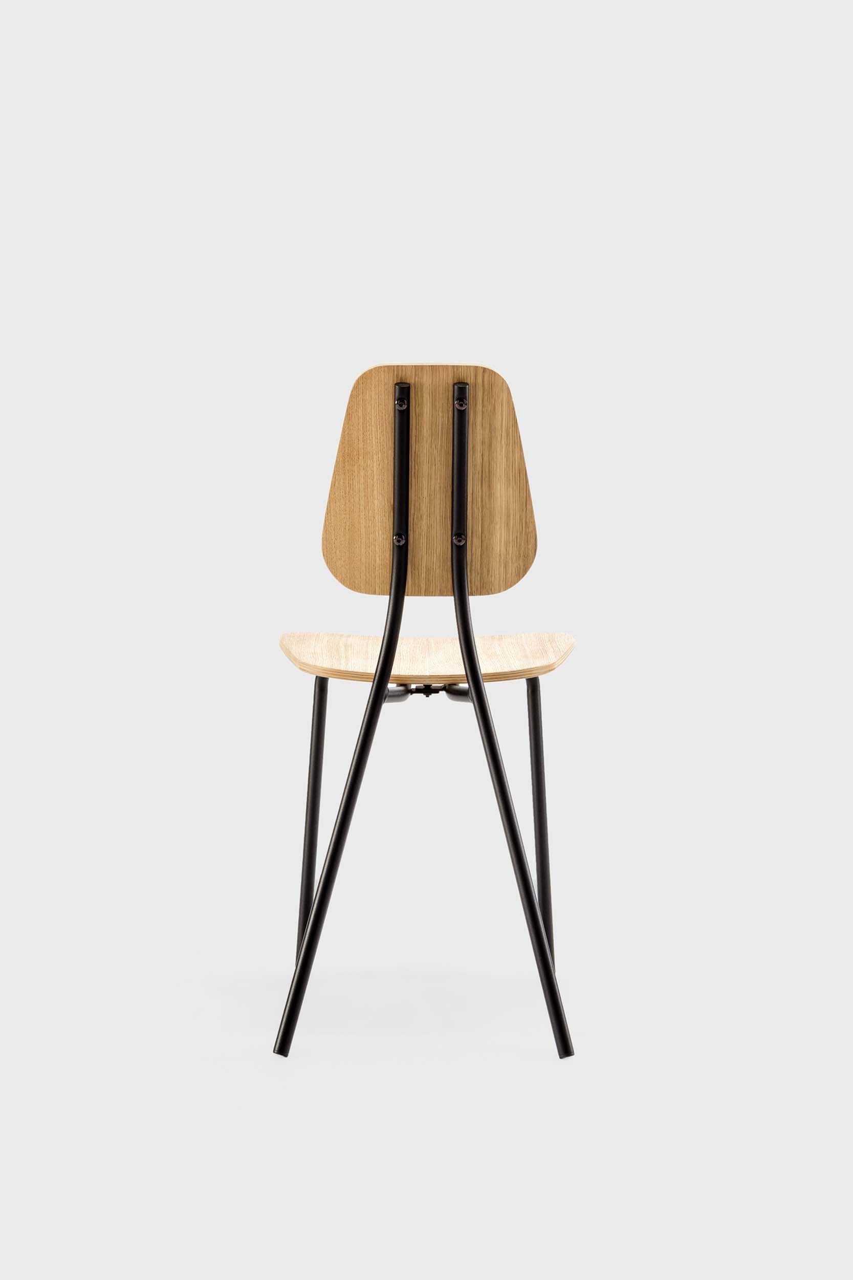 The Hoya Chair features a sleek black metal frame with a veneered plywood seat and backrest, available in natural oil, black, and walnut finishes, showcasing its modern design.