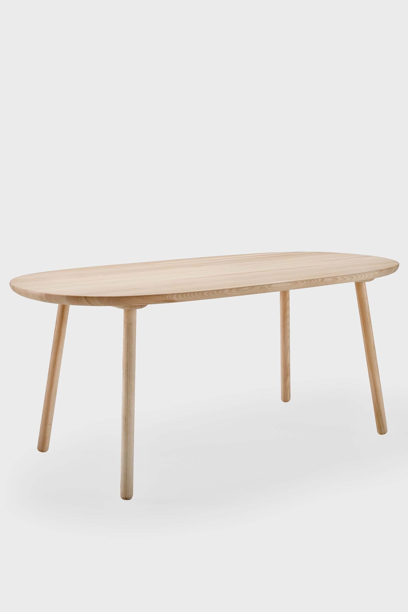 Naïve Dining Table featuring a roundish ash wood tabletop with sturdy legs, showcasing a minimalist design in a cozy dining setting.