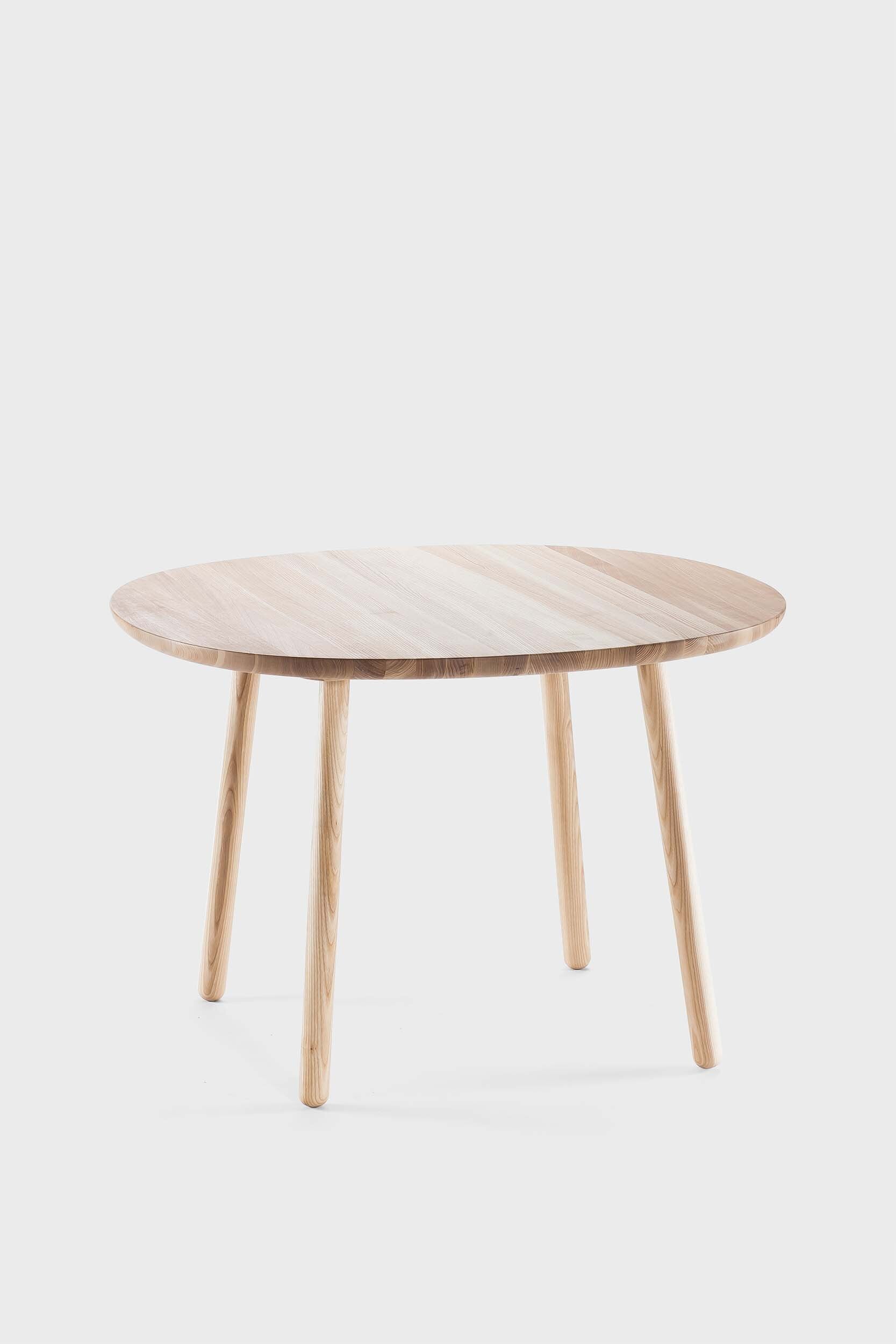 Naïve Dining Table featuring a roundish ash wood tabletop with sturdy legs, showcasing a minimalist design in a cozy dining setting.