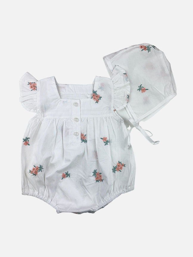 Adeline 2 pc onesie set featuring white cotton fabric with pink and green floral embroidery, ruffle sleeves, and a matching tie bonnet.