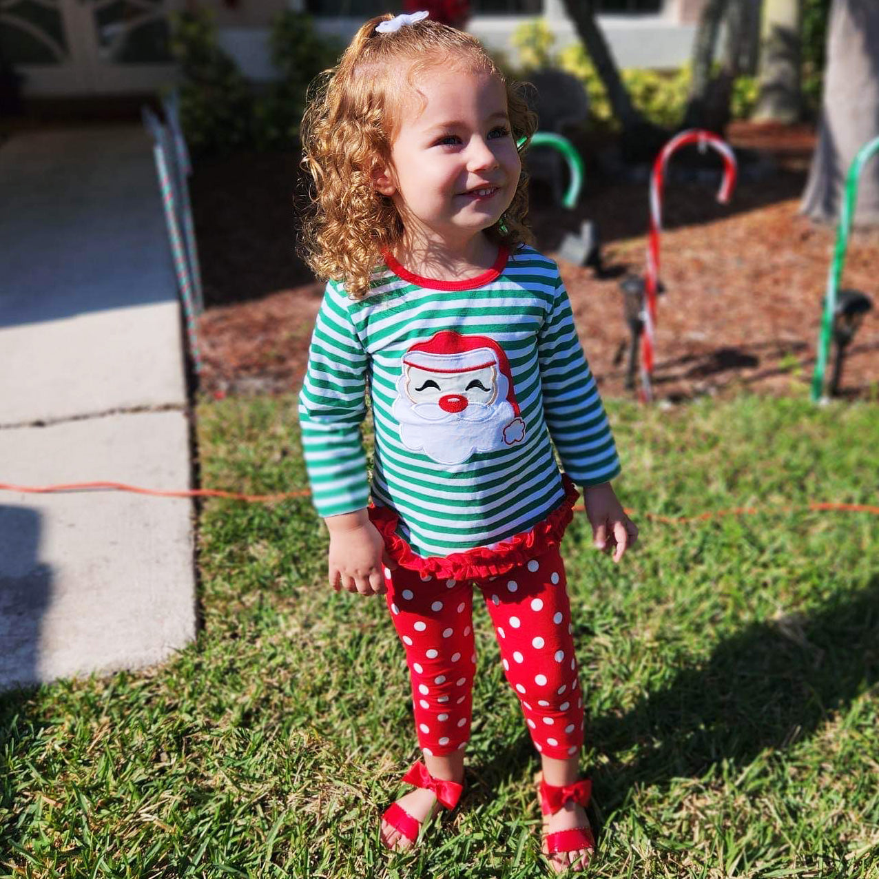 A festive girls' outfit featuring a Santa tunic top with ruffle trim and red polka dot pants, perfect for holiday celebrations.