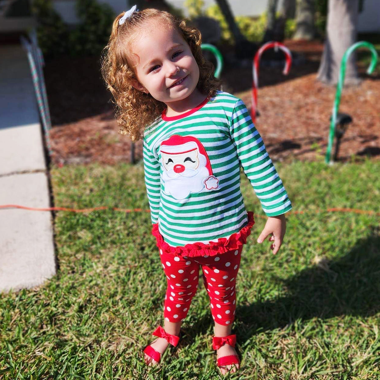 A festive girls' outfit featuring a Santa tunic top with ruffle trim and red polka dot pants, perfect for holiday celebrations.